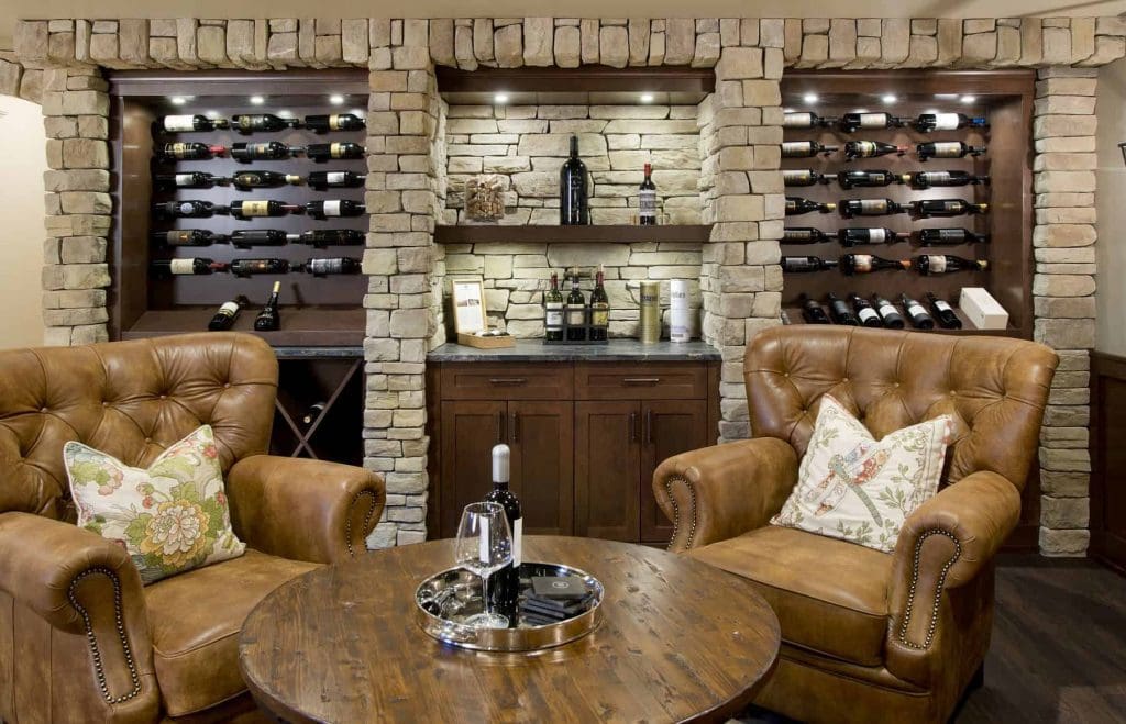 Auburn Bay Wine Room Project By Renova Homes & Renovations Calgary, Alberta stone walls, with custom wine shelves with brown leather chairs fit for a king