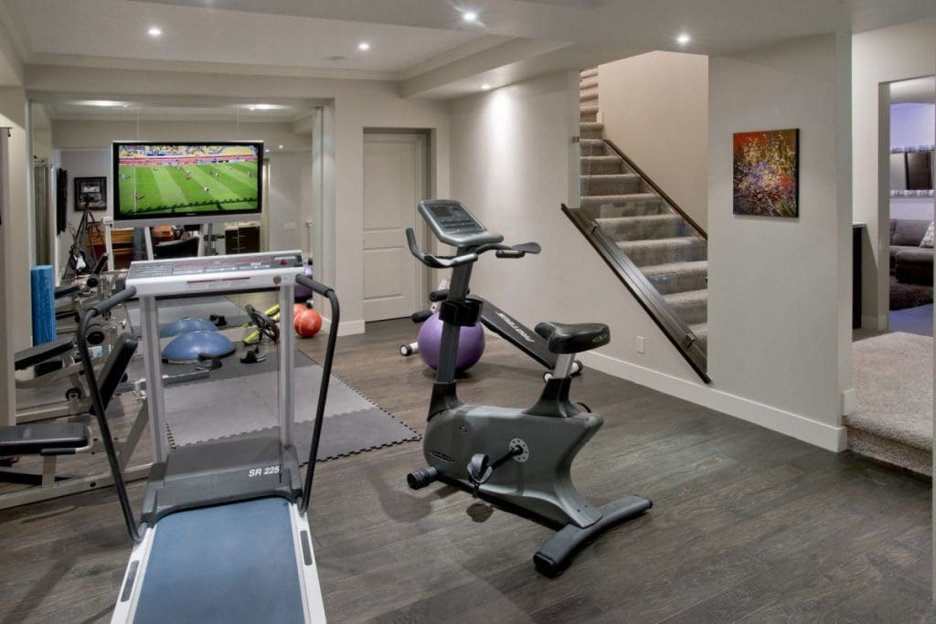 Workout room in basement with laminate flooring by Renova Homes and Renovations