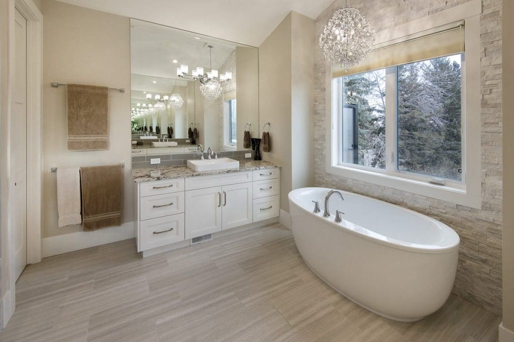 Hounsfield Heights Custom Home By Renova Homes & Renovations Calgary, Alberta master bedroom ensuite with giant soaker bathtub at the foot of a tiled accent wall under a grande chandelier