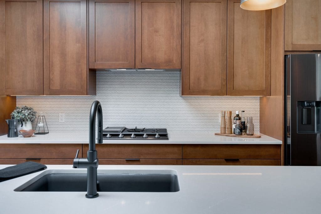 Arbour Lake Kitchen with brown cabinetry and Herringbow tile backsplash by Renova Homes & Renovations In Calgary, Alberta